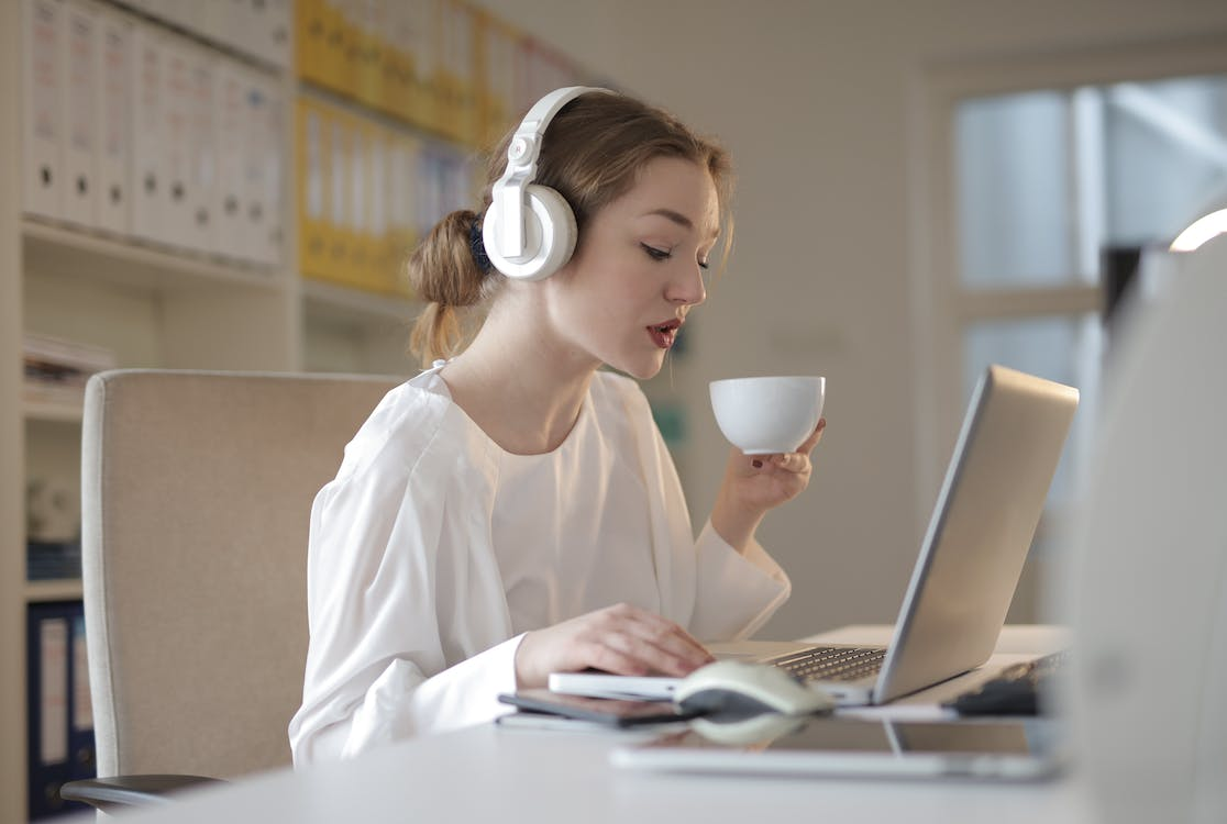 girl listening to music on headphones and sipping tea while working on laptop