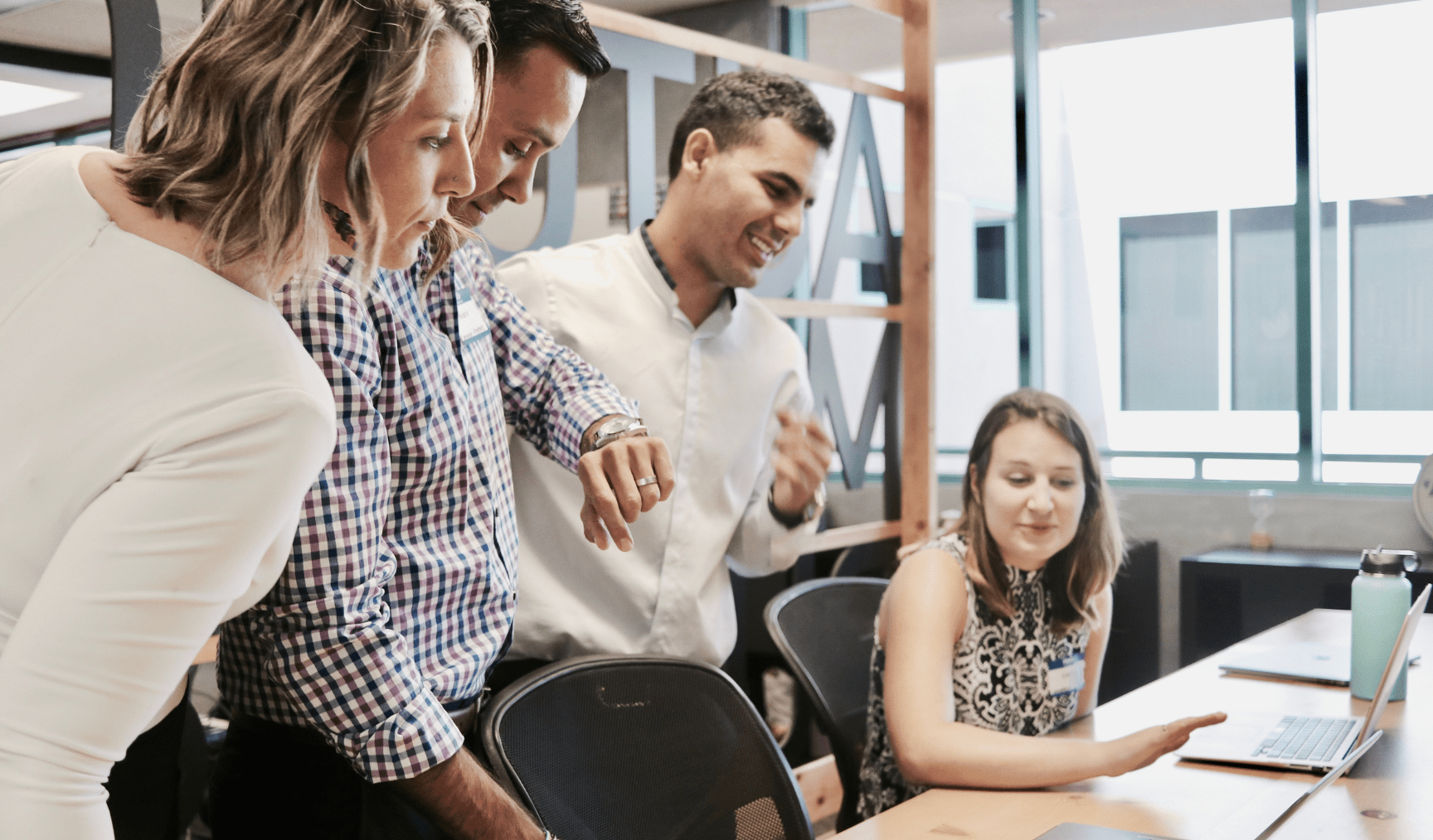 A woman sits at her desk while her colleagues chat to her
