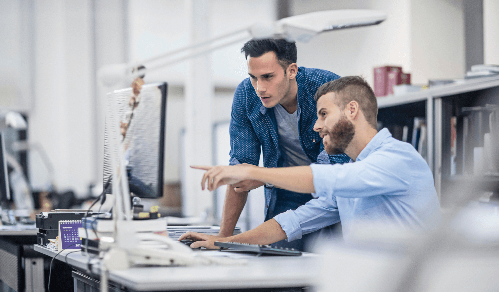 a man pointing something out to another man in an office