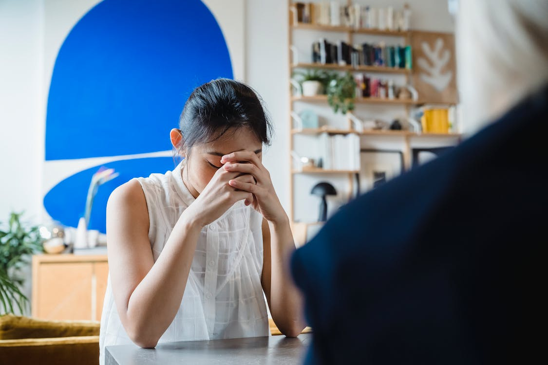 woman seated at a table with her hand bowed down and her hands clasped together