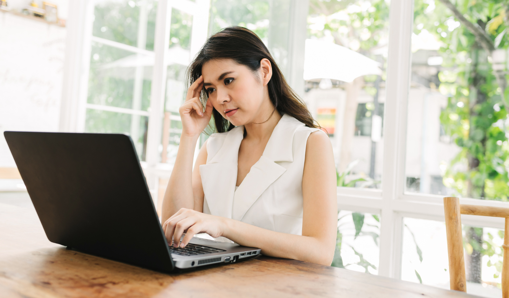 Woman with her hand on her head while looking at her laptop