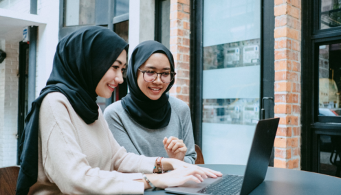 two colleagues chatting and smiling while using a laptop