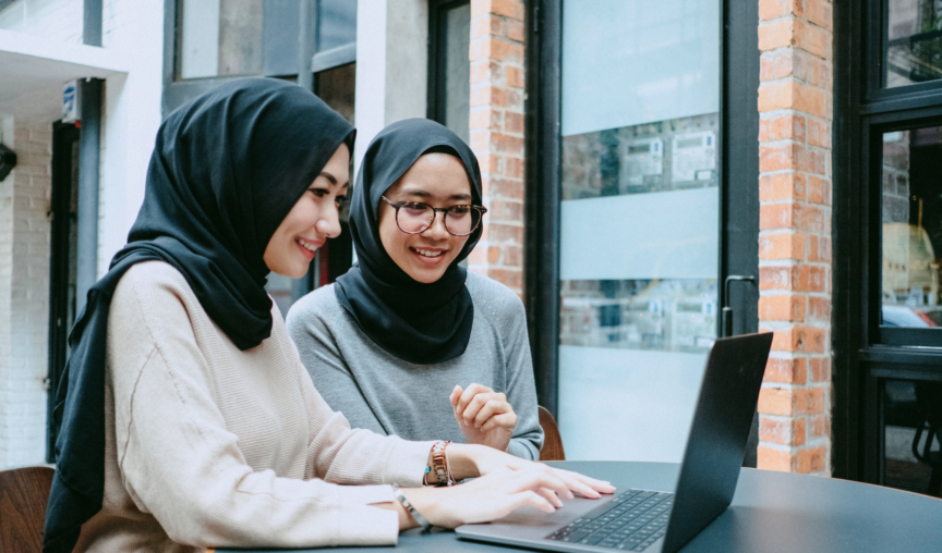two colleagues chatting and smiling while using a laptop