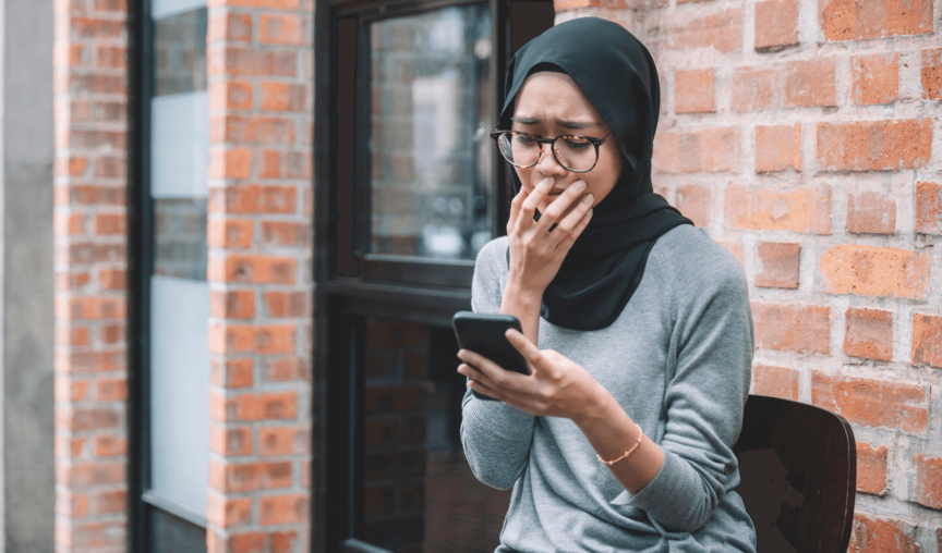 woman in anguish while looking at her phone and covering her mouth