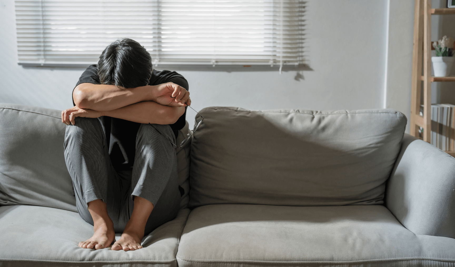 man huddled on the sofa with his head buried in his arms and hugging his knees
