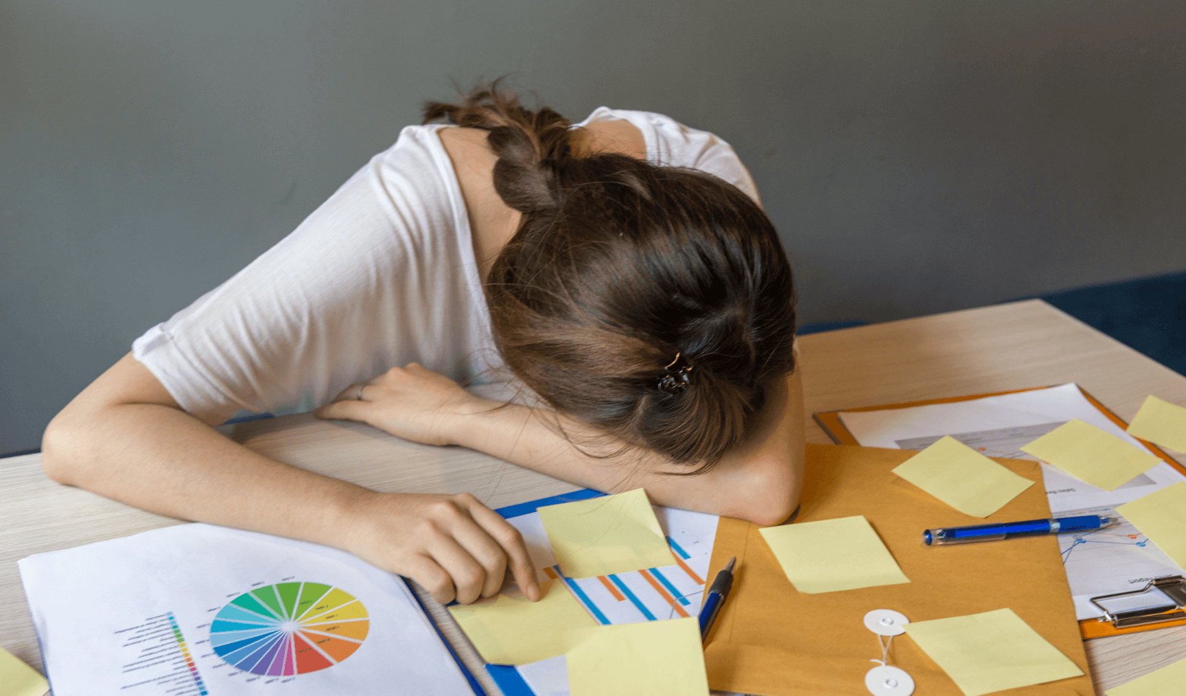 woman lying down face flat on her arms at her work desk