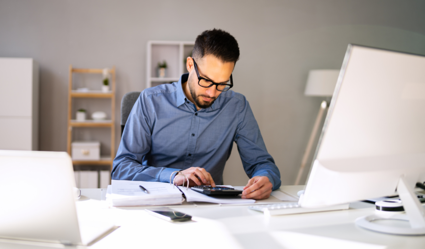 man seated at desk punching numbers into a calculator