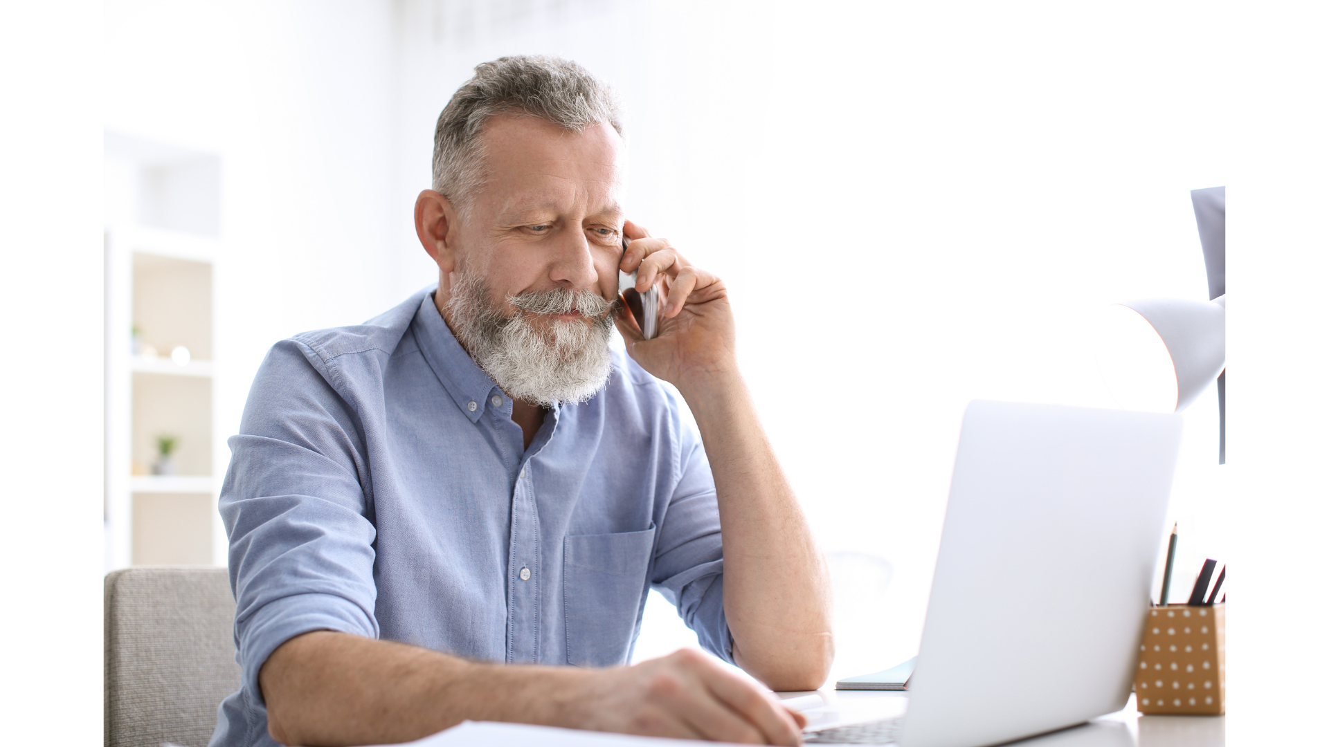 An older man at work on his laptop and phone