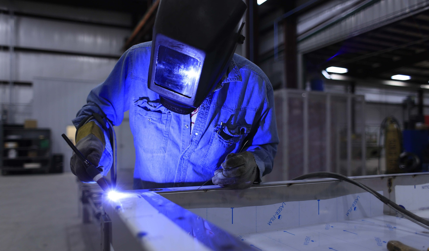 A welder works on a piece of metal, full protective gear on