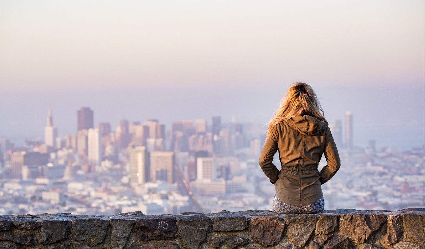 Women sits on a wall overlooking a large city