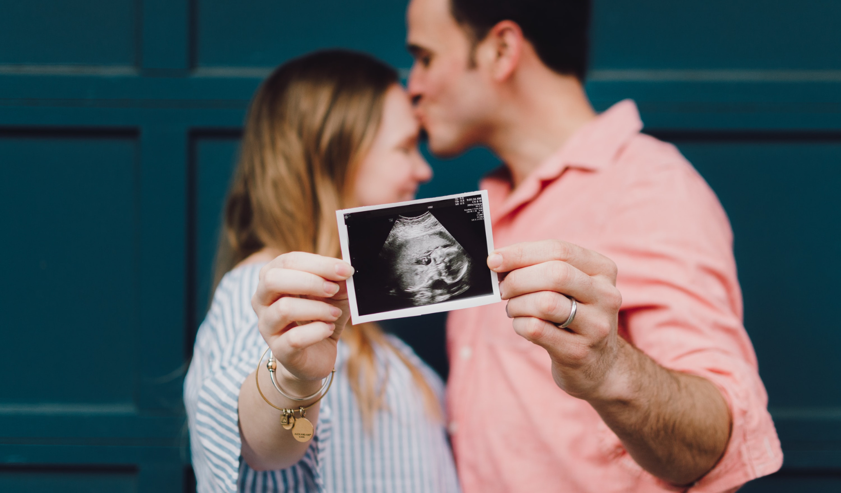 A man and a woman stand facing each other with an ultrasound picture of a baby in the foreground