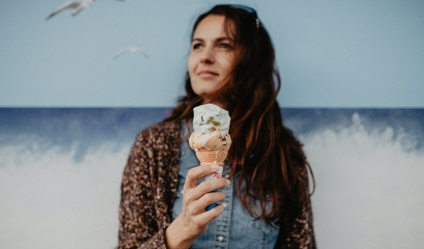 A woman standing on the beach holding an ice cream