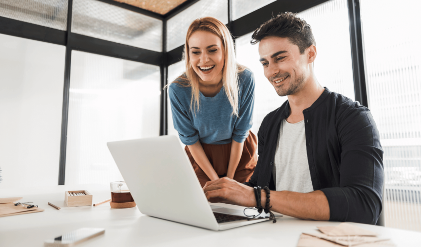 This is an image of 2 people smiling and looking at a laptop.