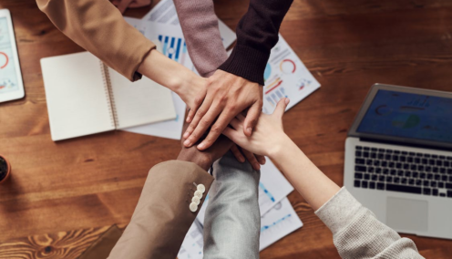 group of diverse employees all putting their hands together in the middle of the table