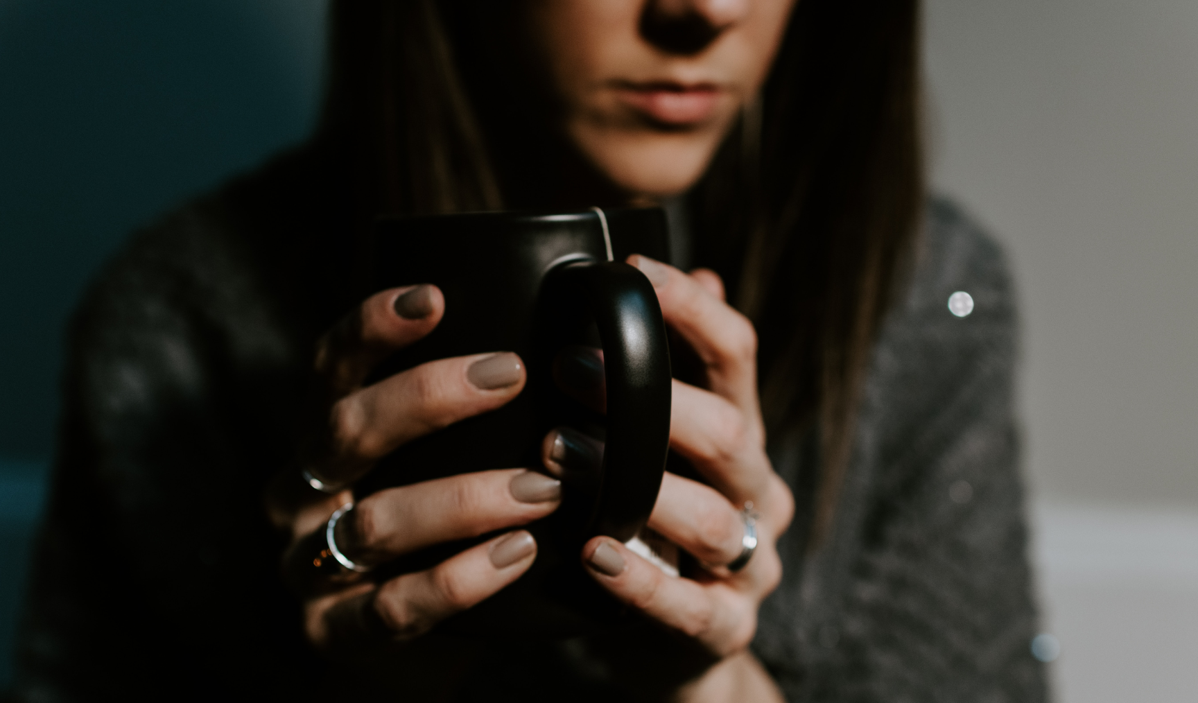 A woman sits with a sombre expression, cradling a mug 