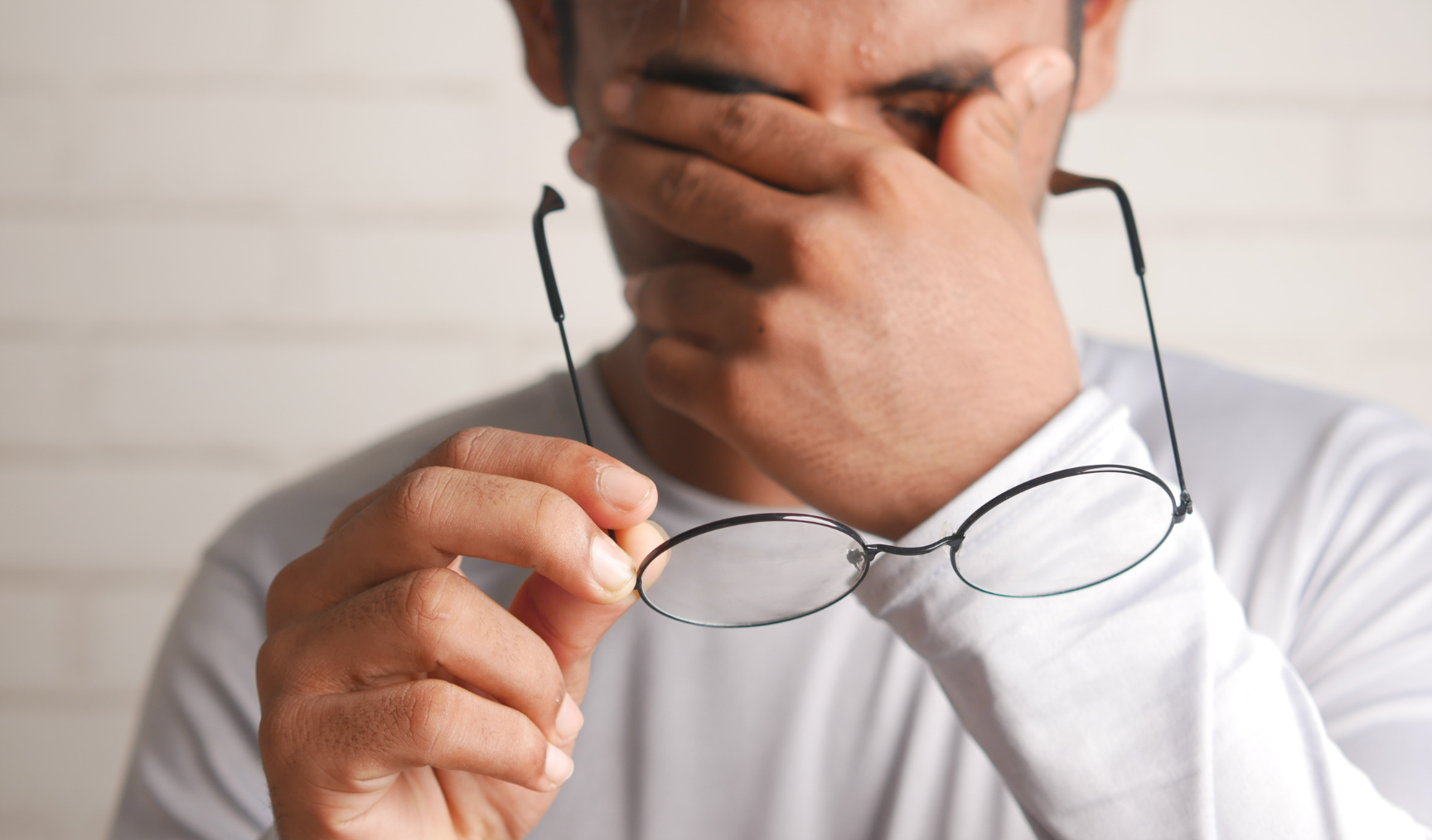 Man is rubbing his eyes, holding his glasses in one hand