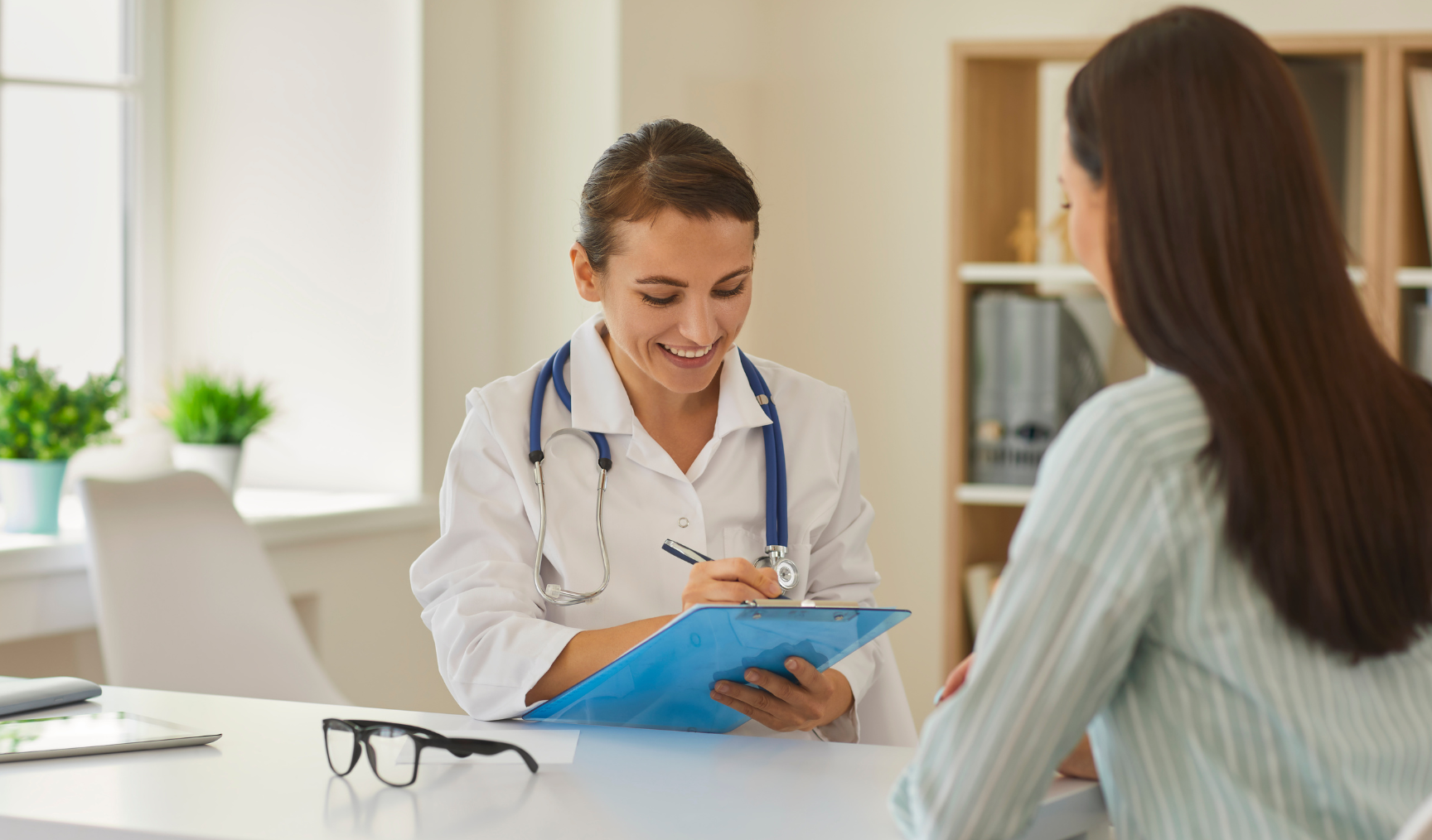 A doctor makes notes on a clipboard in front of a patient