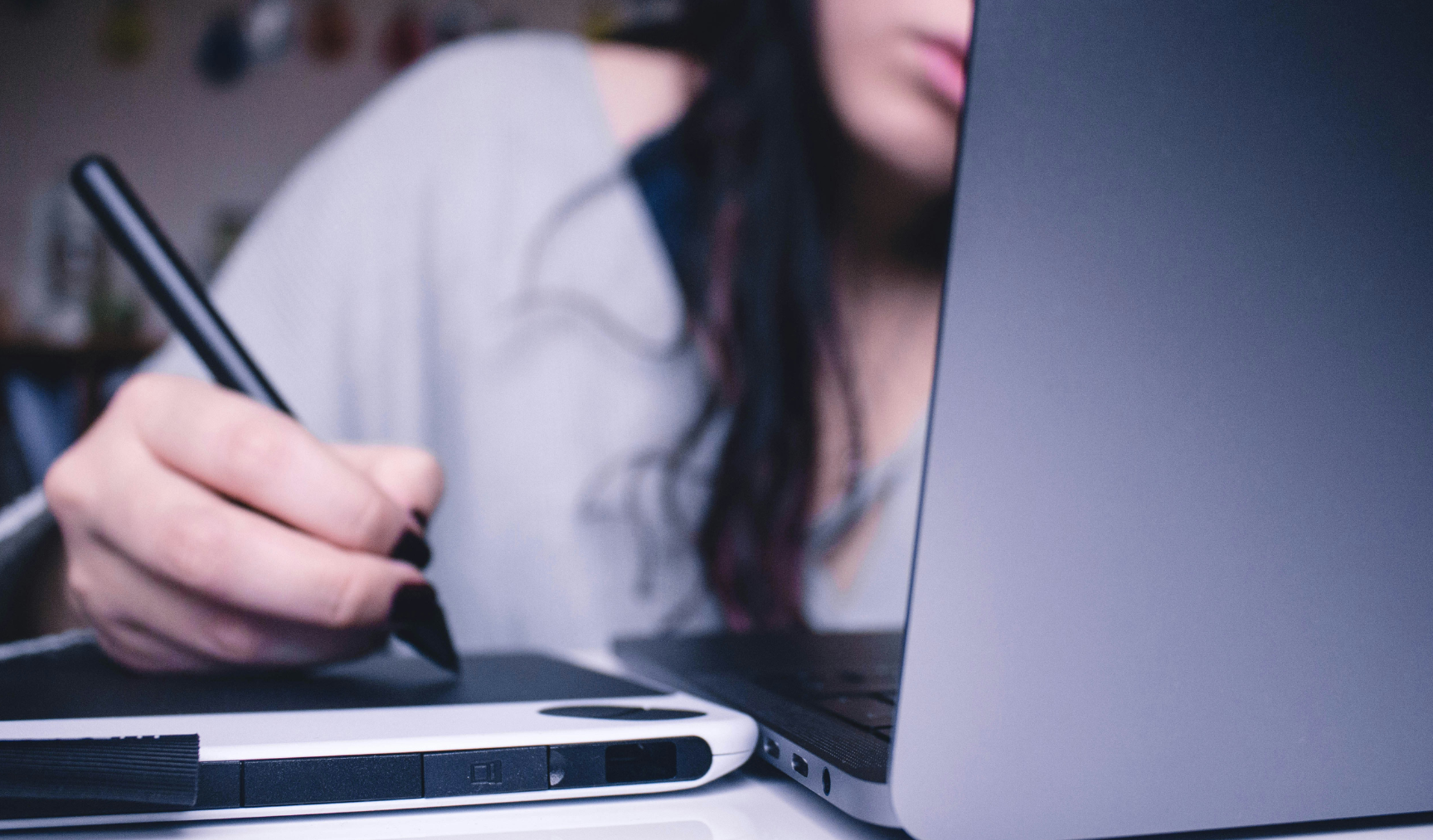 Woman sits at laptop, pen and tablet in hand