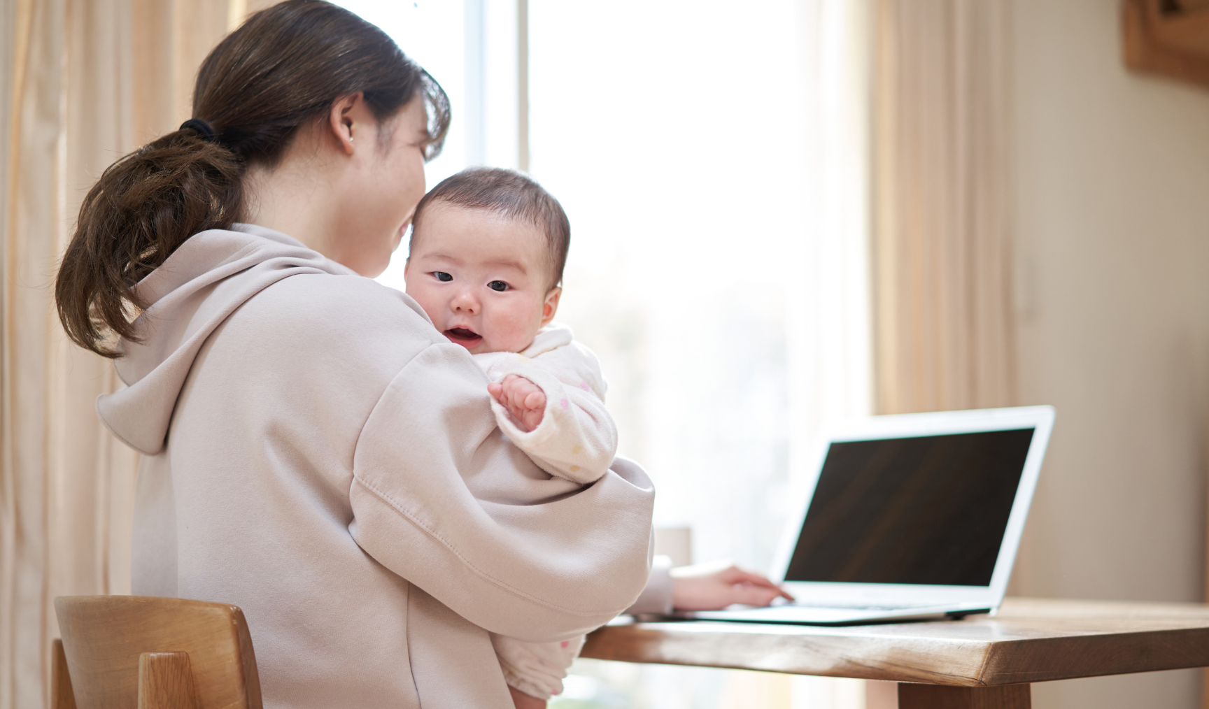mom holding her baby while trying to work at home