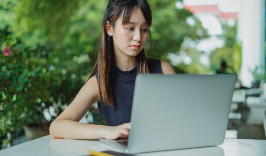 asian woman typing on her laptop in an outdoor space