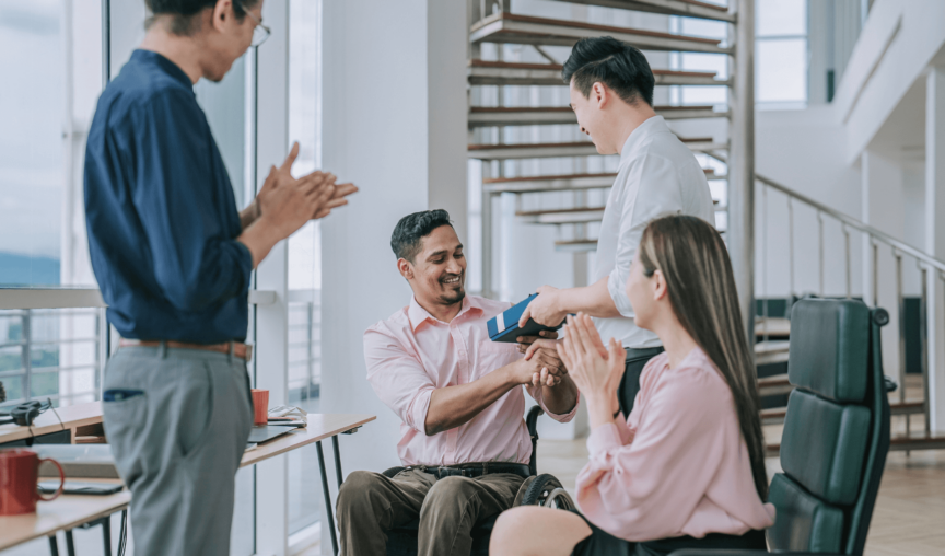 a group of colleagues having a celebration where one man is receiving a gift