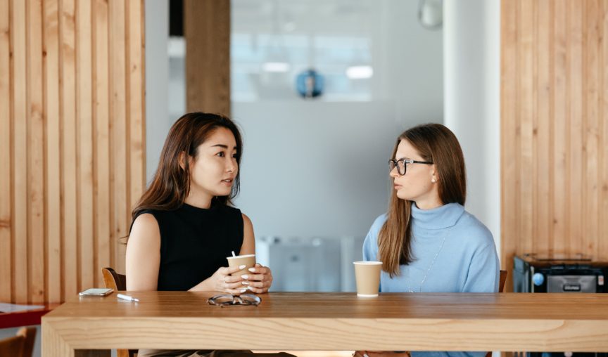 two women seated at a desk talking in the office