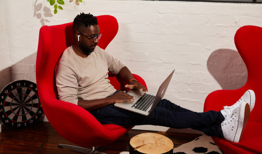 Man sitting in red armchair working on laptop