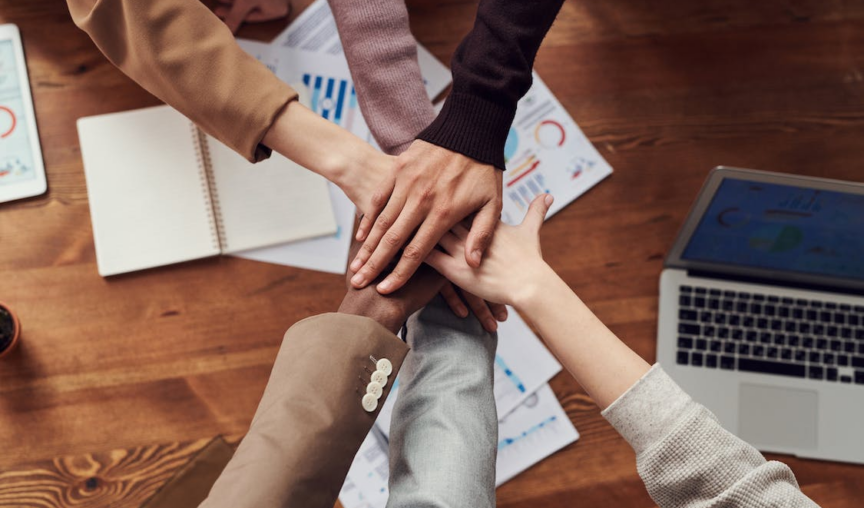 group of diverse employees all putting their hands together in the middle of the table