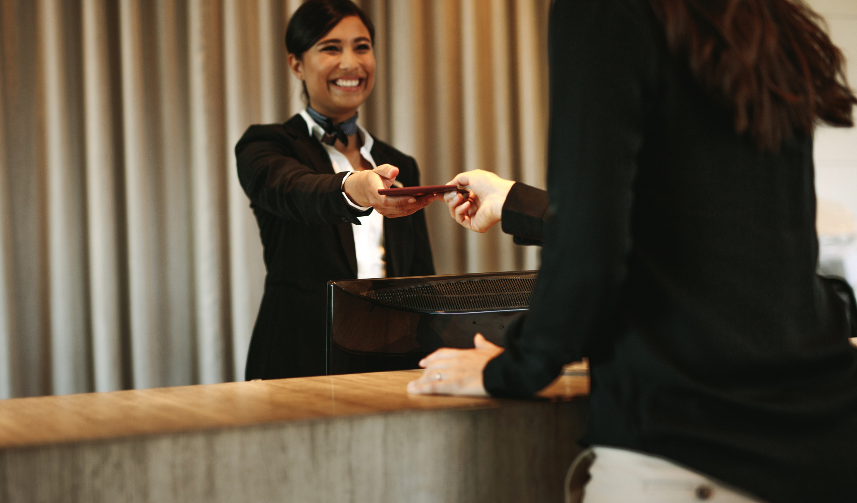 hospitality worker at front desk passing a document to a guest