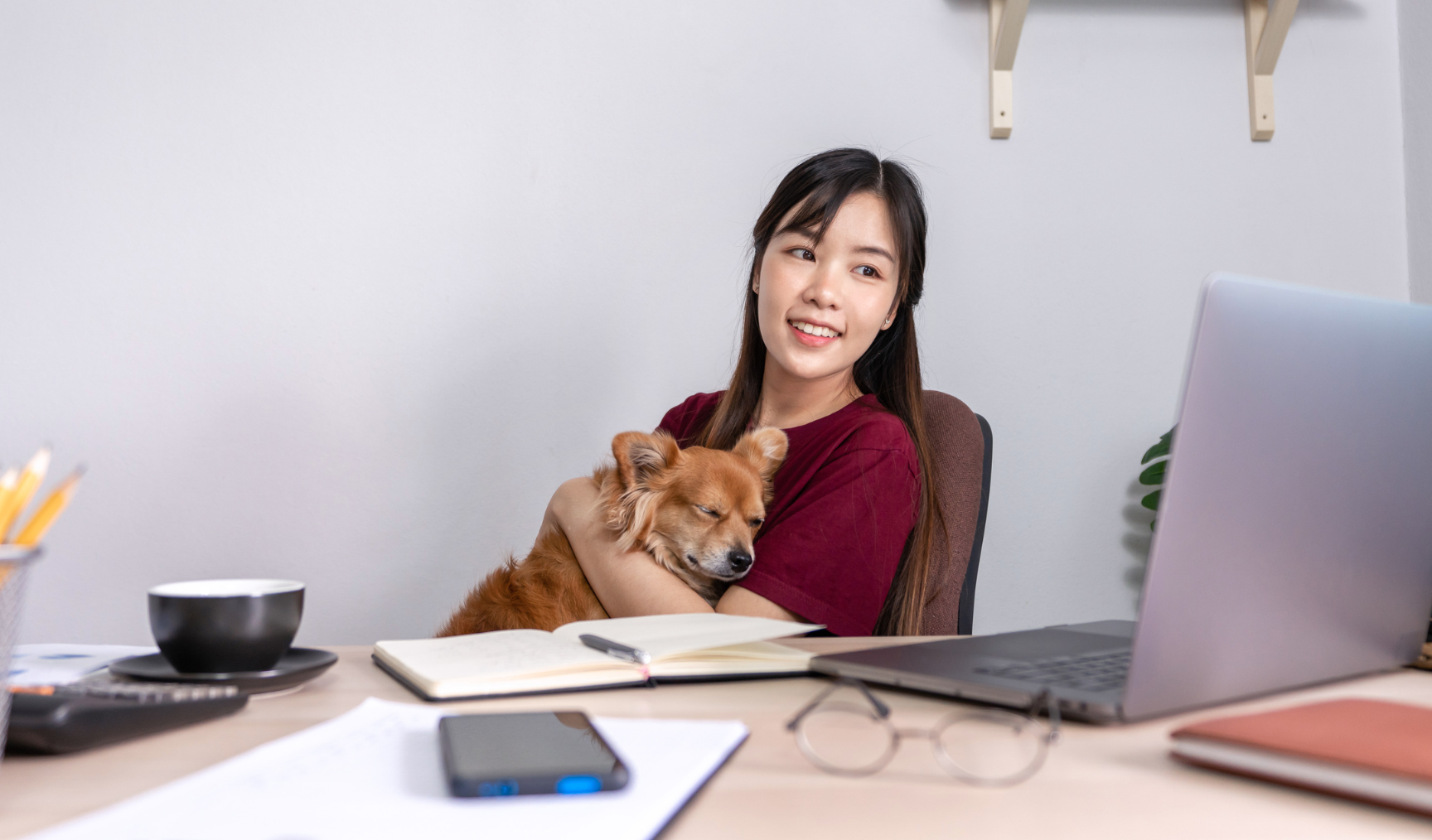 Woman hugging her dog while seated at her work desk