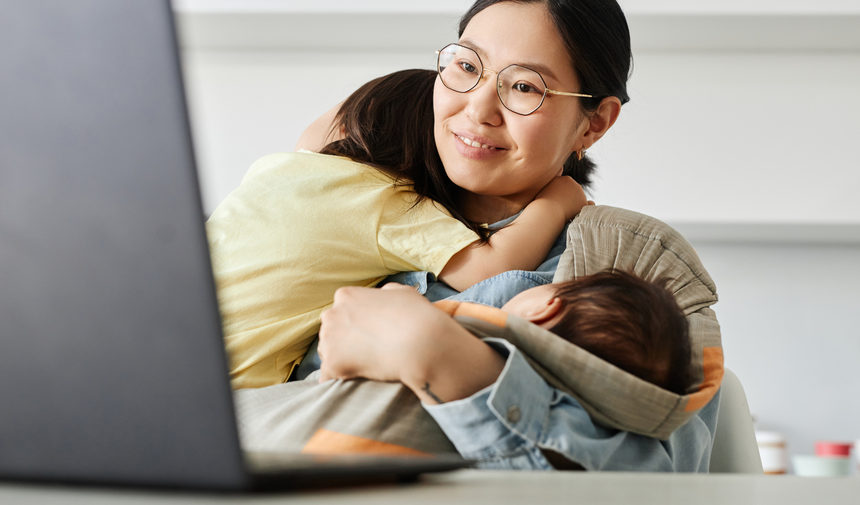 mom carrying her kids while looking at her laptop