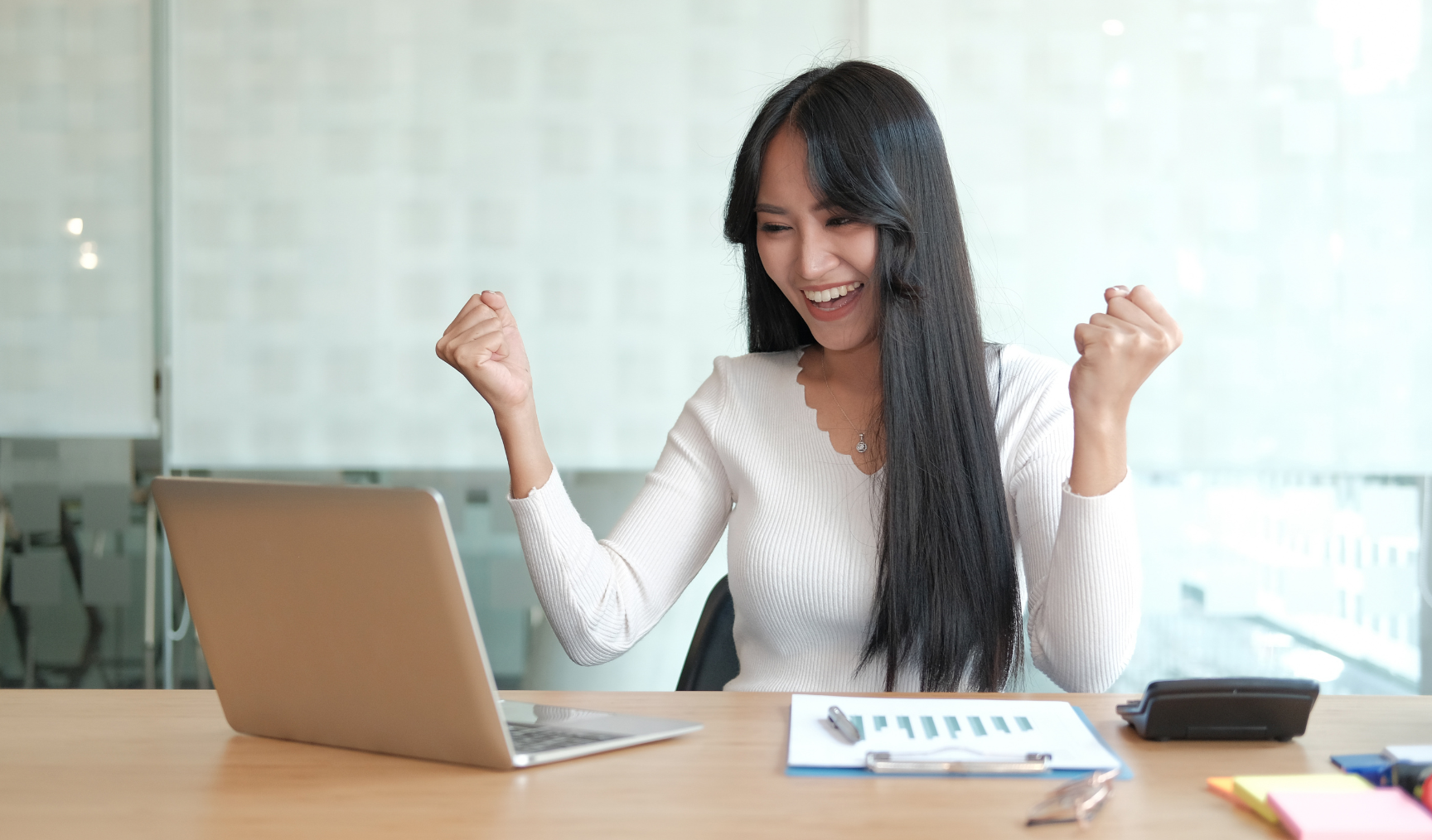woman with raised fists and laughing in joy while staring at her laptop