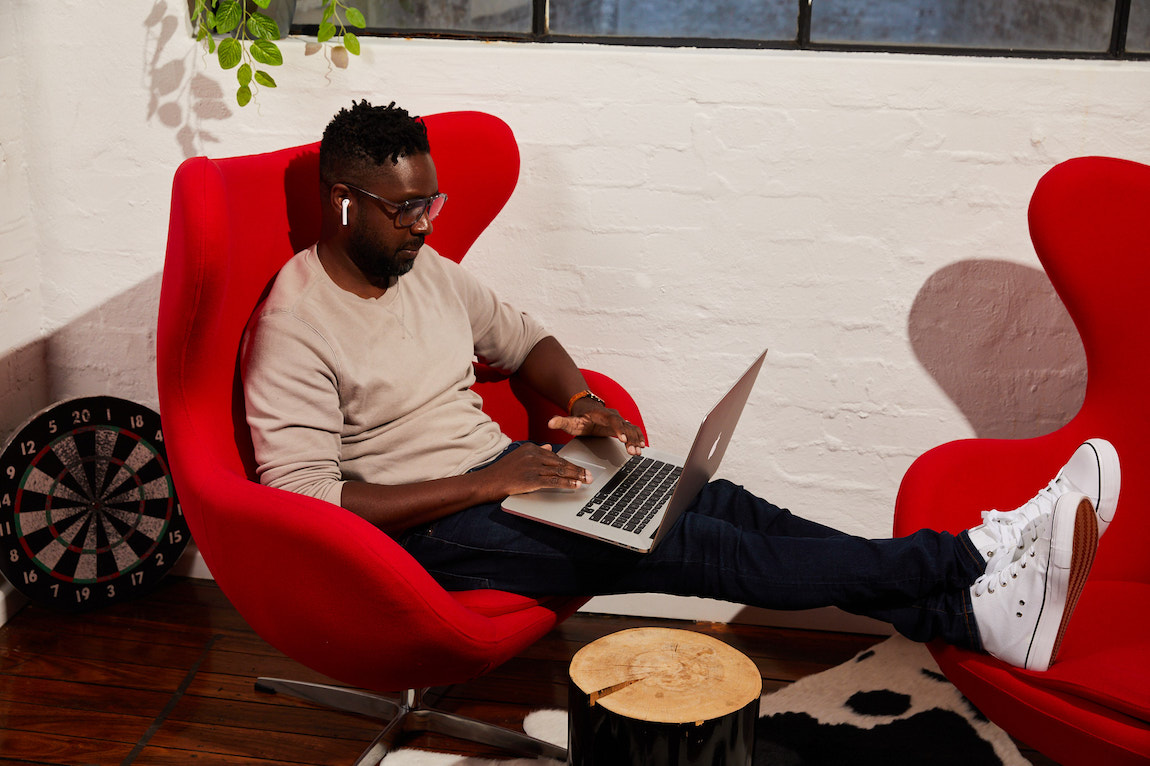 Man sitting in red armchair working on laptop