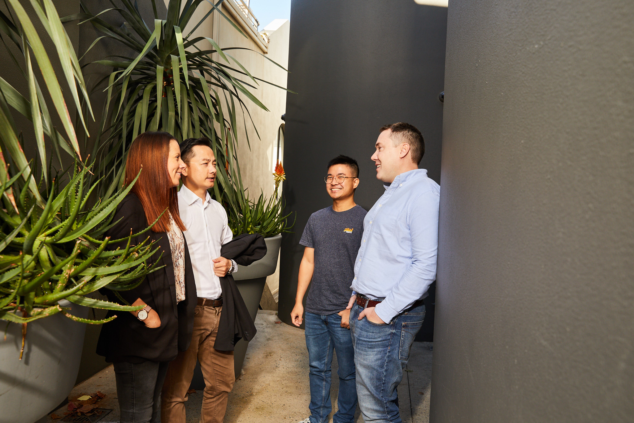 Four people standing in a corridor with plants, facing each other and smiling