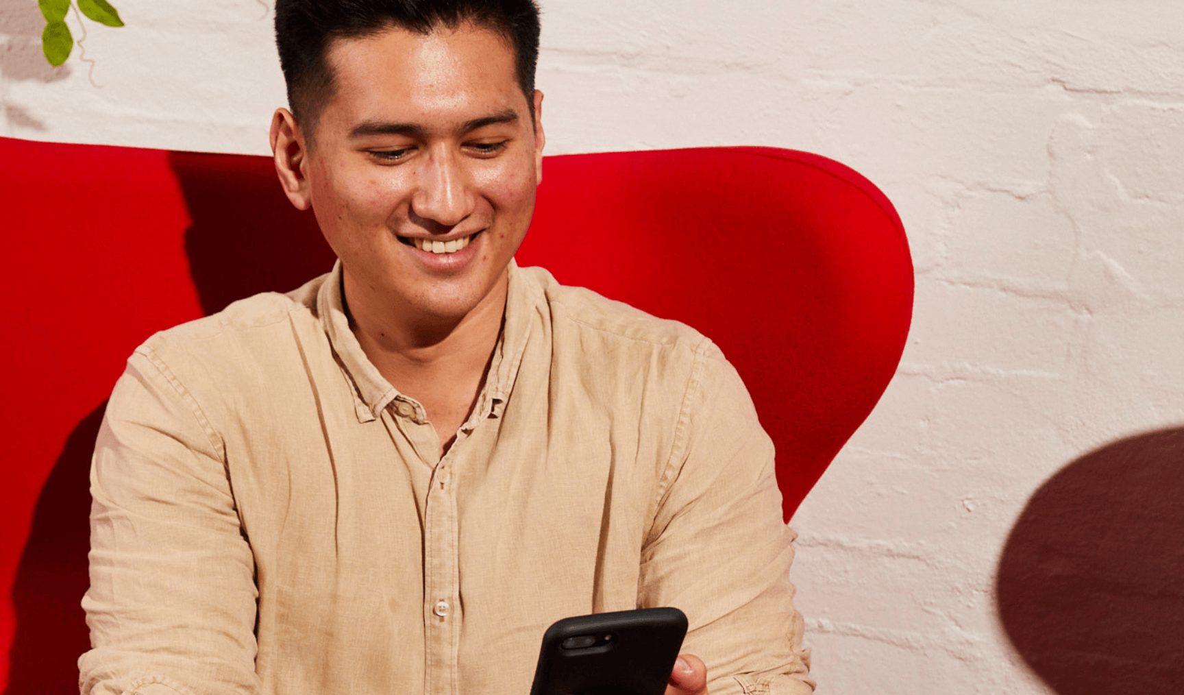 Man sitting in red chair smiling at mobile phone